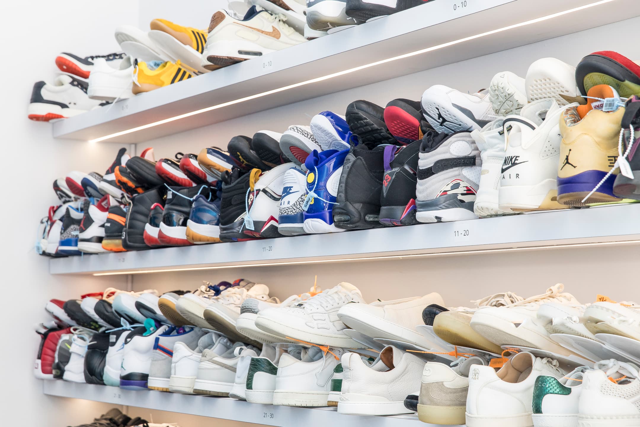 A wall of sneakers organized on illuminated shelves at a Sneakky Klean store.